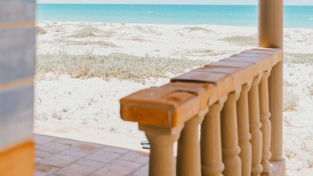 A beach view from a covered area with a wooden railing. - The Suites at Rocky Point 2 (Puerto Peñasco)