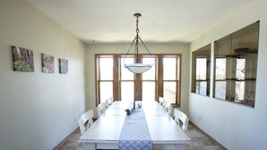 A dining room with a white table, chairs, and a patterned runner. There are large windows and a hanging light fixture. - One Minute to Road America - Close to PGA Golfing (Plymouth)