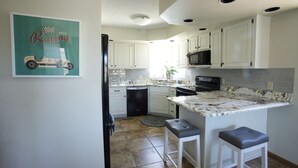 A modern kitchen with white cabinets, a marble countertop, and a built-in microwave. There are two bar stools and a small island with a sink. - One Minute to Road America - Close to PGA Golfing (Plymouth)