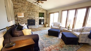 A living room with a stone fireplace, a ceiling fan, and large windows. - One Minute to Road America - Close to PGA Golfing (Plymouth)