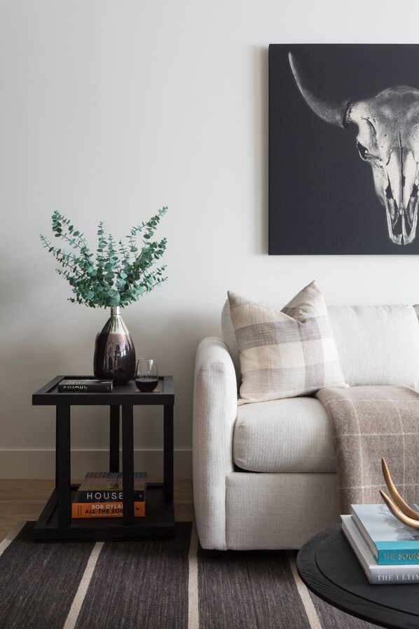 A living room with a sofa, a small side table with a vase and books, a framed picture on the wall, and a rug. - Outpost: One Town Hill 306 - Base of Snow King Mtn (Jackson)