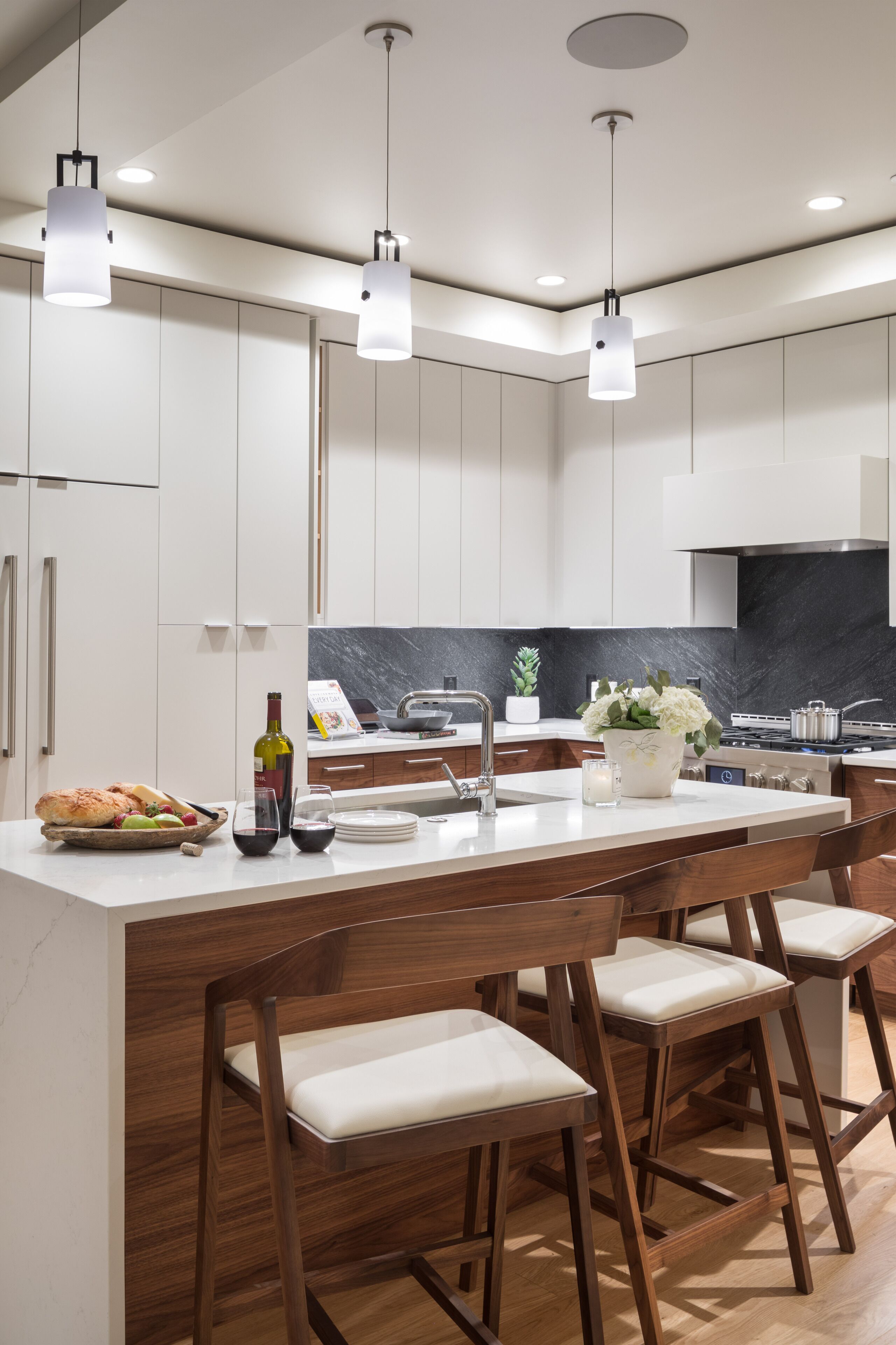A modern kitchen with white cabinets, a marble backsplash, and a central island with bar stools.
