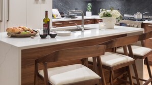 Une cuisine moderne avec des meubles blancs, un pare-feu en marbre et un îlot central doté de tabourets de bar.