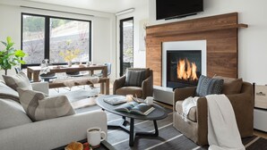 Un salon moderne doté d’une cheminée, de sièges confortables et d’un coin repas offrant une vue sur l’extérieur.