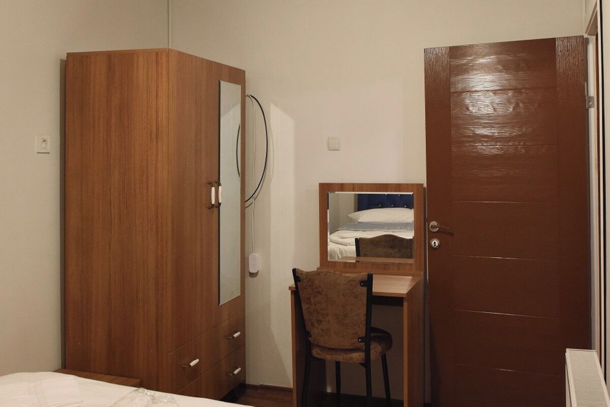 Un dormitorio con cama, armario, escritorio y silla, además de una puerta.
