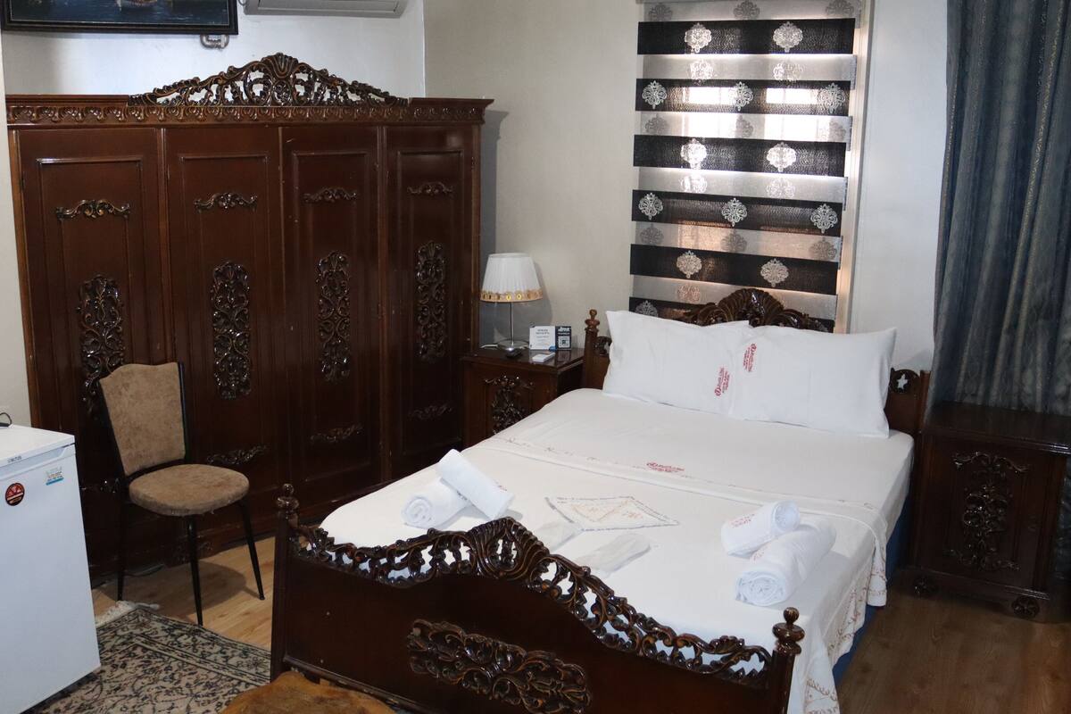 Una habitación de hotel con cama, armario, escritorio con lámpara y una silla.