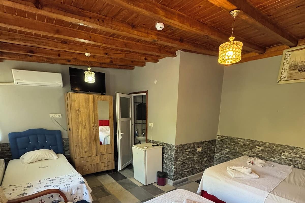 Una habitación de hotel con dos camas, techo de madera, televisión y baño con lavamanos y espejo.
