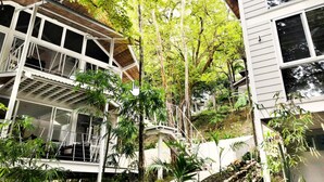 A multi-level house with a covered outdoor area, surrounded by lush greenery and trees. - MarAmar Bungalows (Cóbano)