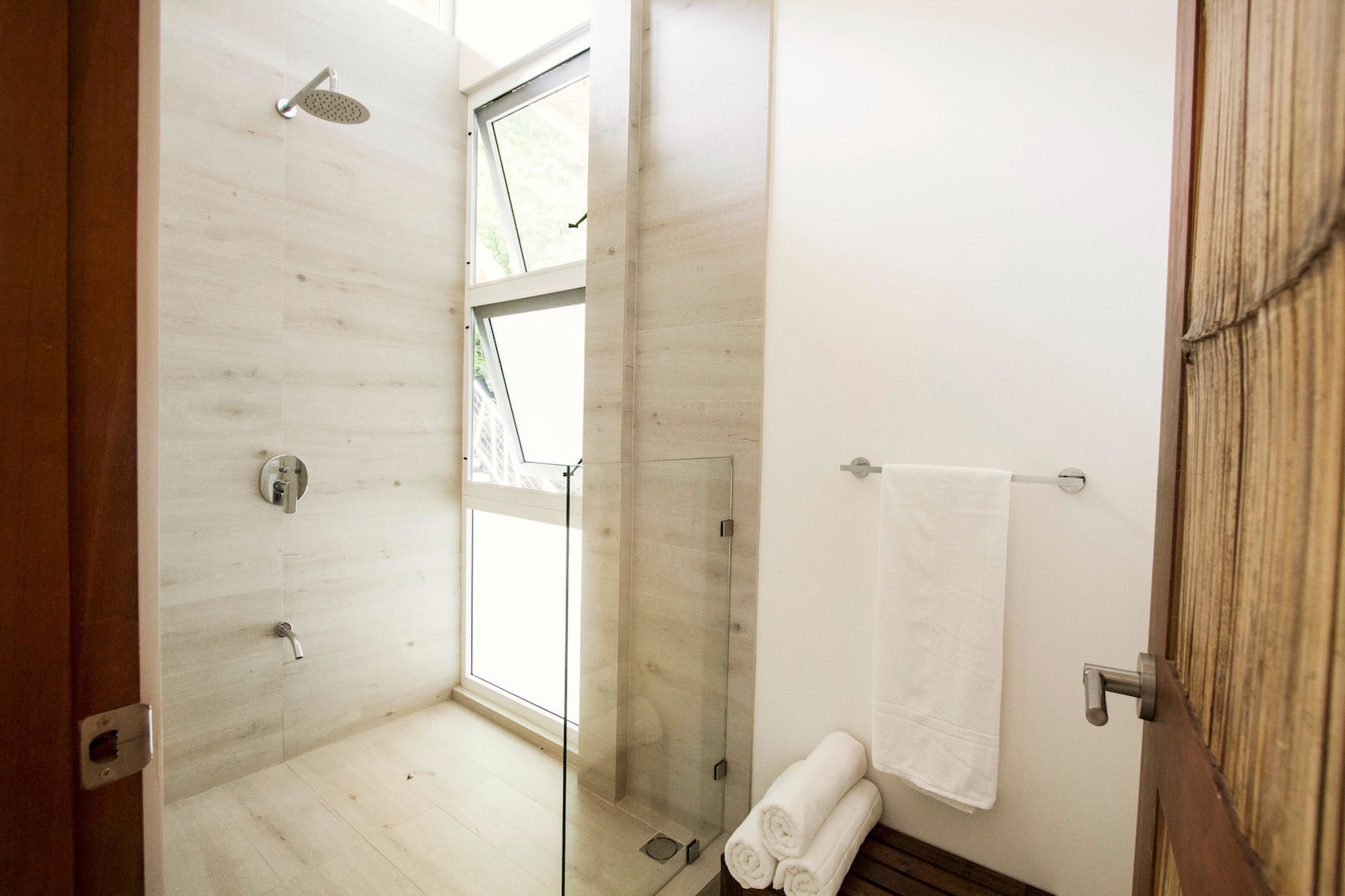 Une salle de bain moderne avec une douche à parois de verre, une fenêtre visible et une porte en bois.