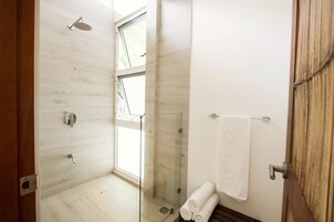 Un baño moderno con ducha envuelta en vidrio, ventana visible y puerta de madera.