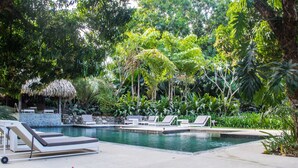 A pool area with lounge chairs and a thatched-roof structure. - MarAmar Bungalows (Cóbano)