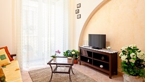 Een woonkamer met een bank, een salontafel, een televisie op een houten standaard en potplanten.