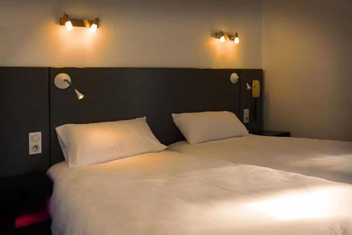 A hotel room with two beds, each with white linens, and wall-mounted lighting fixtures.