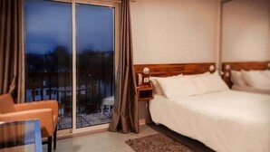 A hotel room with a bed, a chair, a nightstand, and a view through a sliding door. - Hôtel Bonnet (Saint-Pee-sur-Nivelle)