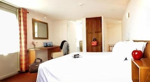 A hotel room with a bed, a desk, a chair, a suitcase, and a red apple on the nightstand. - Hôtel Bonnet (Saint-Pee-sur-Nivelle)