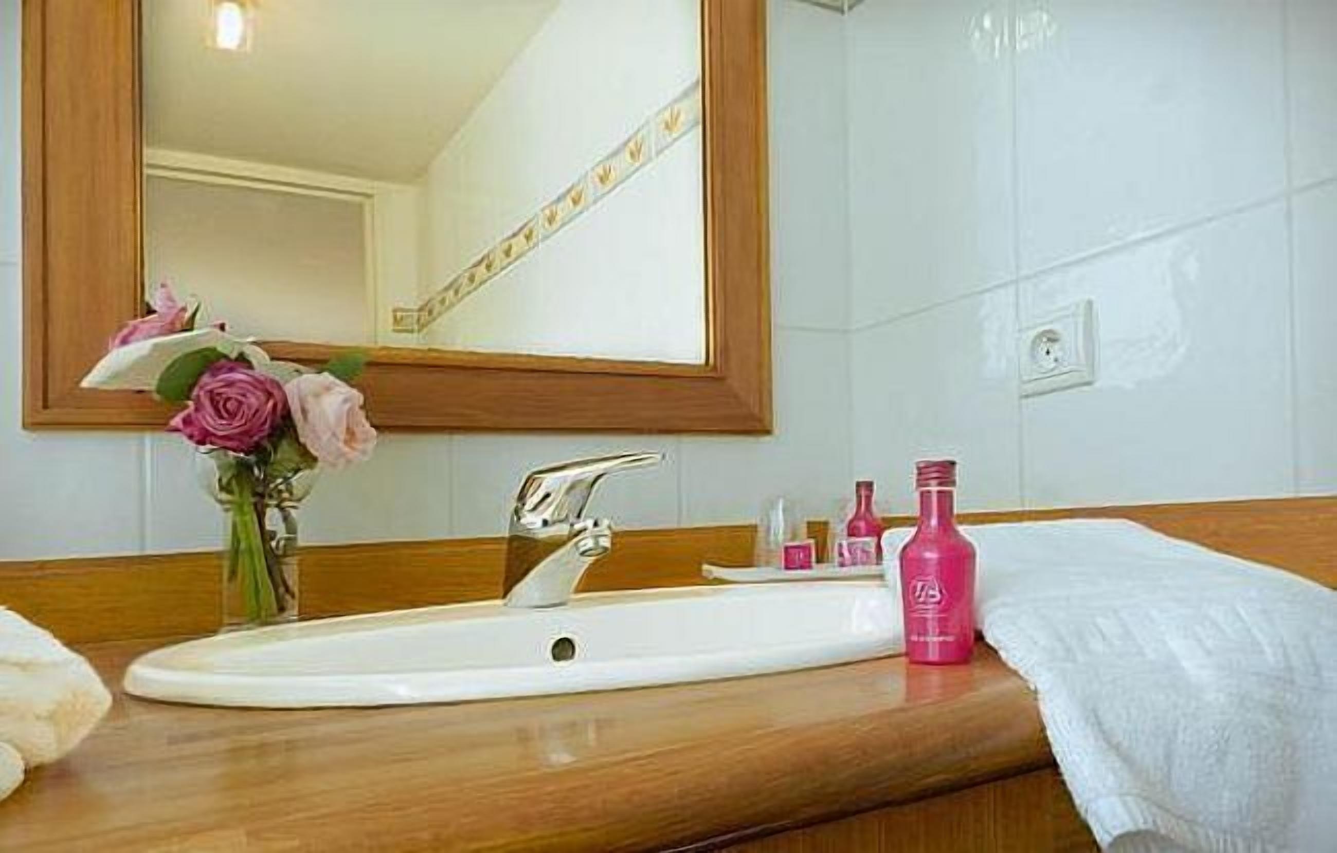 Un baño con un lavabo blanco, un espejo y un florero con flores rosas.