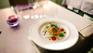 A white plate with a dish of food, a fork, and a glass of red liquid on a table. - Hôtel Bonnet (Saint-Pee-sur-Nivelle)