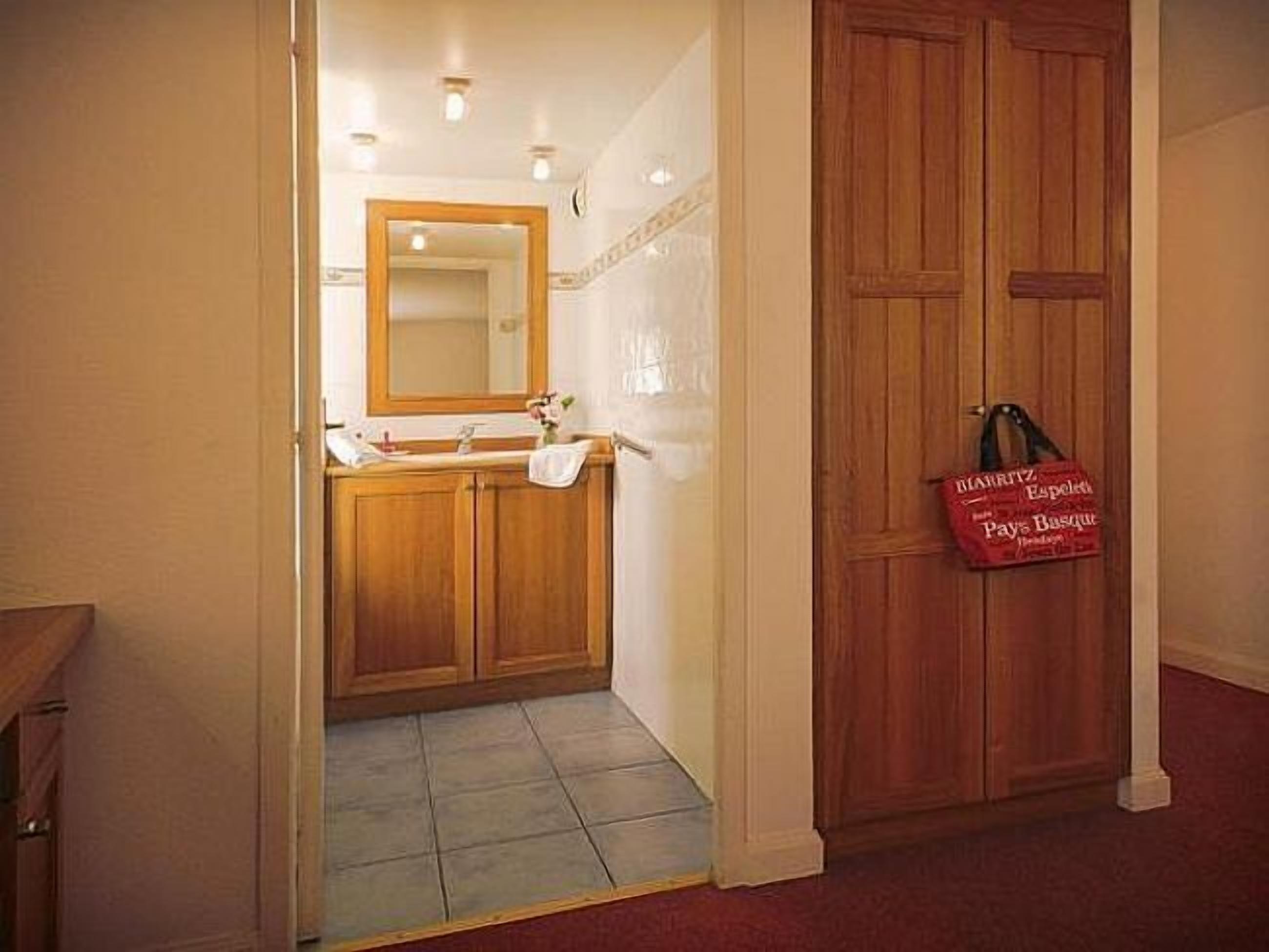 A bathroom with wooden cabinets, a sink, and a mirror. There is a red bag hanging on the door.