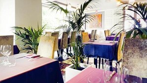 A restaurant interior with tables covered in blue tablecloths, chairs with yellow cushions, and potted plants. - Hôtel Bonnet (Saint-Pee-sur-Nivelle)
