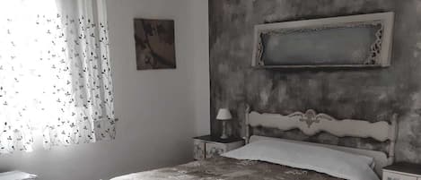 A bedroom with a bed, a nightstand, a dresser, a chandelier, and a window with curtains.