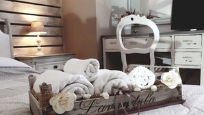 A neatly made bed with a decorative tray of rolled towels and flowers, a white dresser, and a mirror above it. - Grotta dei Puntali (Carini)