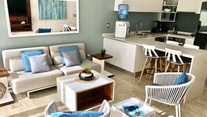 A modern living room with a sofa, coffee table, and chairs, a kitchen with a water dispenser, and a dining area with bar stools. - MOB 205 by Riviera Rentals (Playa del Carmen)