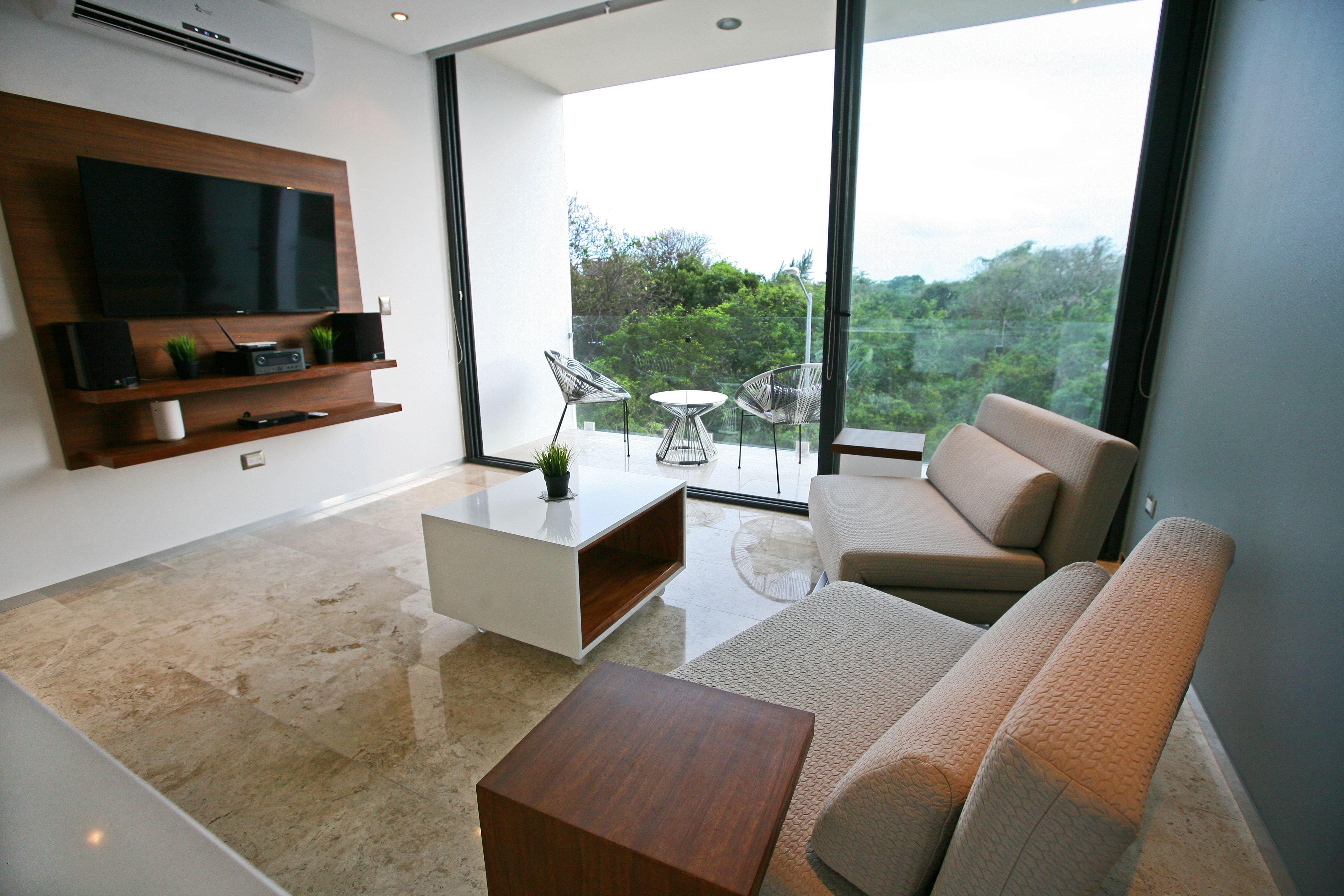A modern living room with a flat-screen TV, a coffee table, a sofa, and a dining area with chairs.