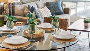 A dining area with a glass table set for four, surrounded by a sofa and a window with blinds. - Gorgeous Ocean Views Family Vacation Condo - Kahana Sunset C1 (Lahaina)
