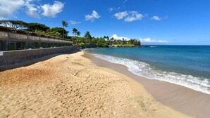 A beach with a clear blue sky, sandy shore, and a building with a balcony overlooking the sea. - Gorgeous Ocean Views Family Vacation Condo - Kahana Sunset C1 (Lahaina)