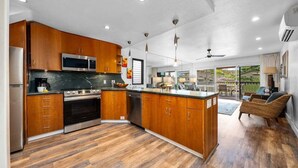A modern kitchen with wooden cabinets, stainless steel appliances, and a large island. - Gorgeous Ocean Views Family Vacation Condo - Kahana Sunset C1 (Lahaina)