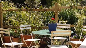 An outdoor seating area with a round table and four chairs, surrounded by potted plants and a wooden fence.