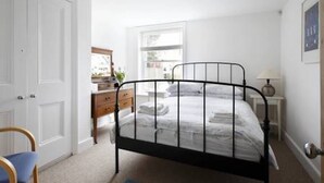 A bedroom with a metal bed frame, white walls, a wooden dresser, and a window with natural light.