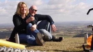 Two people sitting on a grassy hill with a panoramic view.