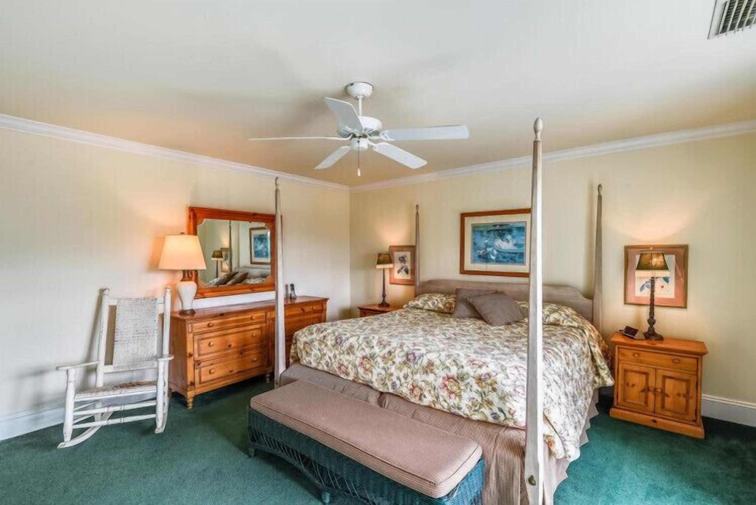 Um quarto com uma cama de dossel, um aparador de madeira, uma poltrona de balanço e um banco.