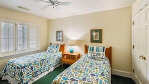 Un dormitorio con dos camas individuales, un ventilador de techo, una mesita de noche con lámpara y una puerta.