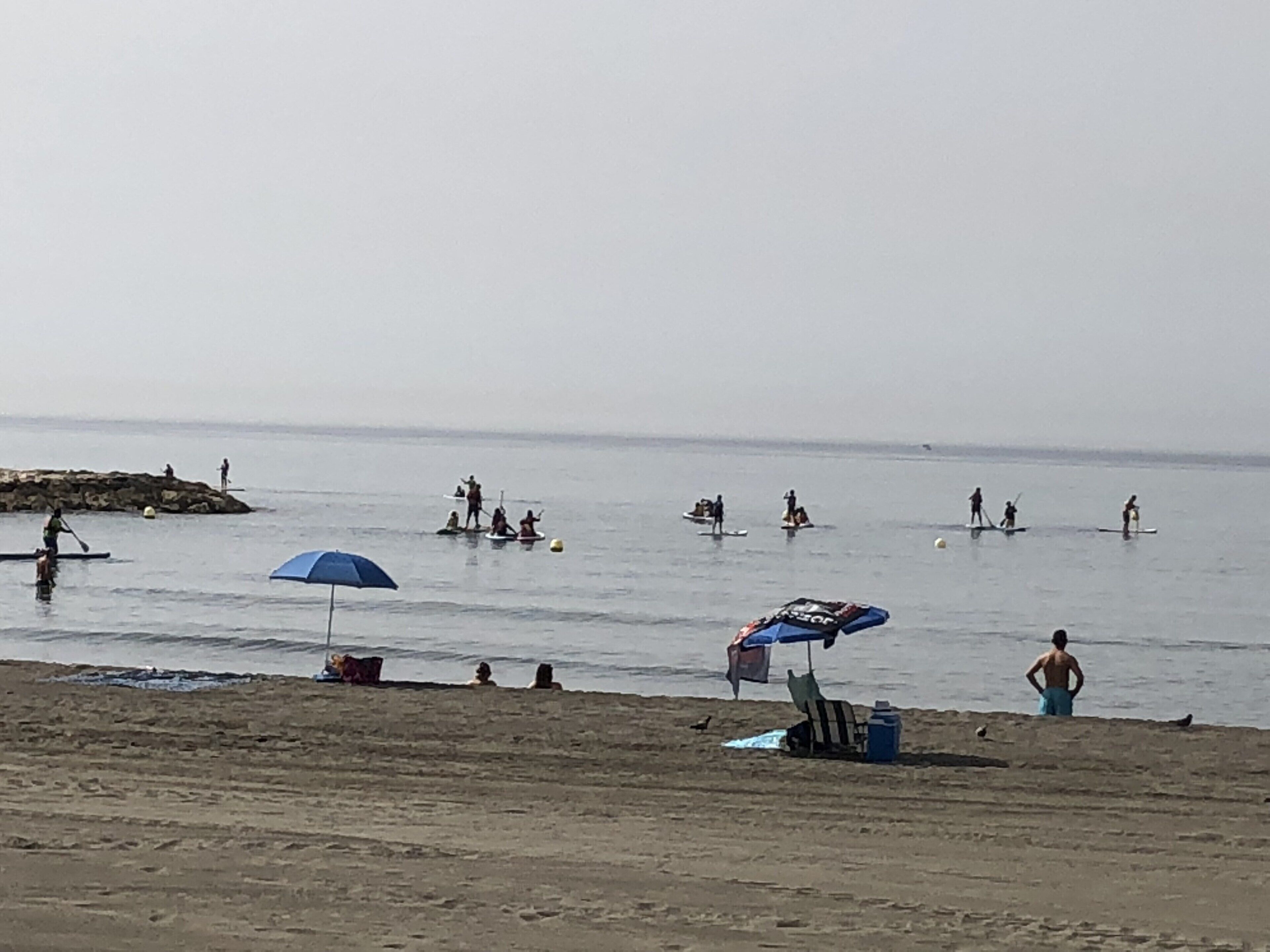 A beach with people engaging in water activities, umbrellas, and beach chairs.