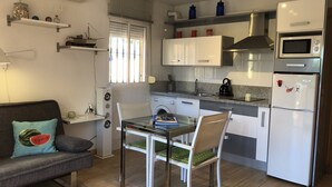 Une cuisine compacte comprenant une table à manger, des chaises, un canapé avec un coussin à motif de pastèque et un réfrigérateur.