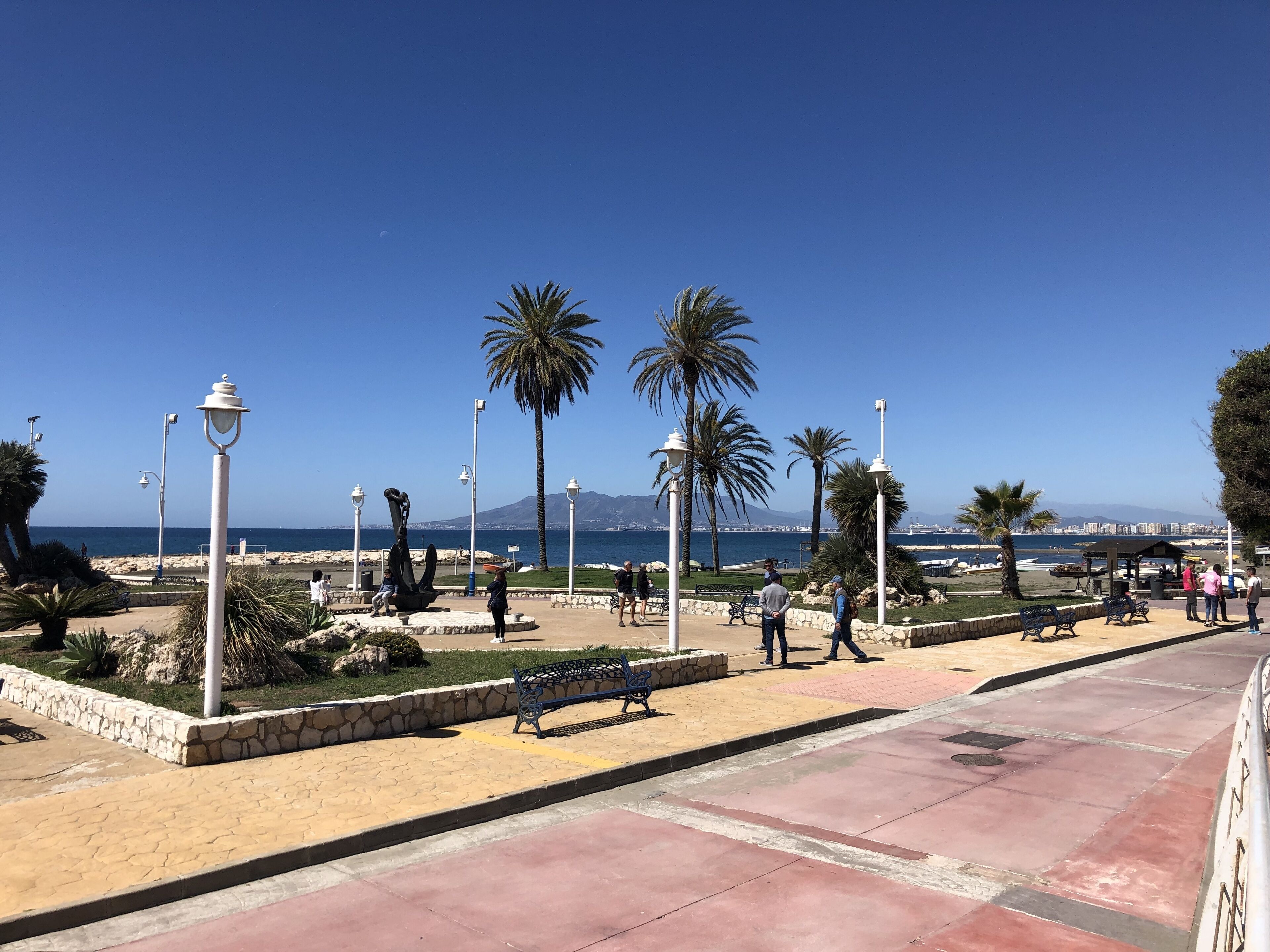 En kystpromenade med bænke, palmer og frit udsyn til havet.
