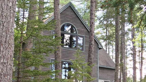 A cabin with a gabled roof, large windows, and a wooden deck. - Comfortable lake home on pristine Beech Hill Pond (Otis)