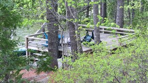 A wooden deck with a bench and a table, surrounded by trees and overlooking a body of water. - Comfortable lake home on pristine Beech Hill Pond (Otis)
