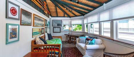 A cozy room with a wooden ceiling, a white sofa, wicker chairs, a wooden table, and framed pictures on the walls.