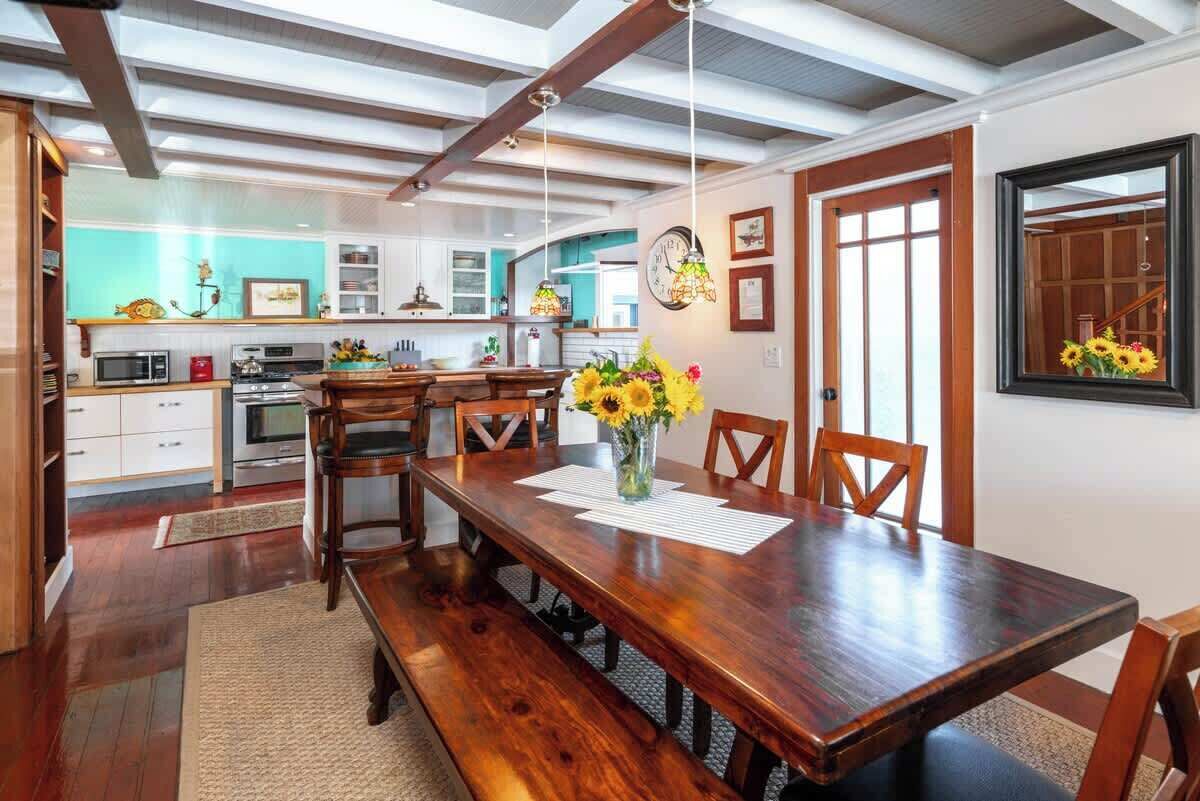 A spacious dining area with a wooden table and benches, a kitchen in the background, and a clock on the wall.