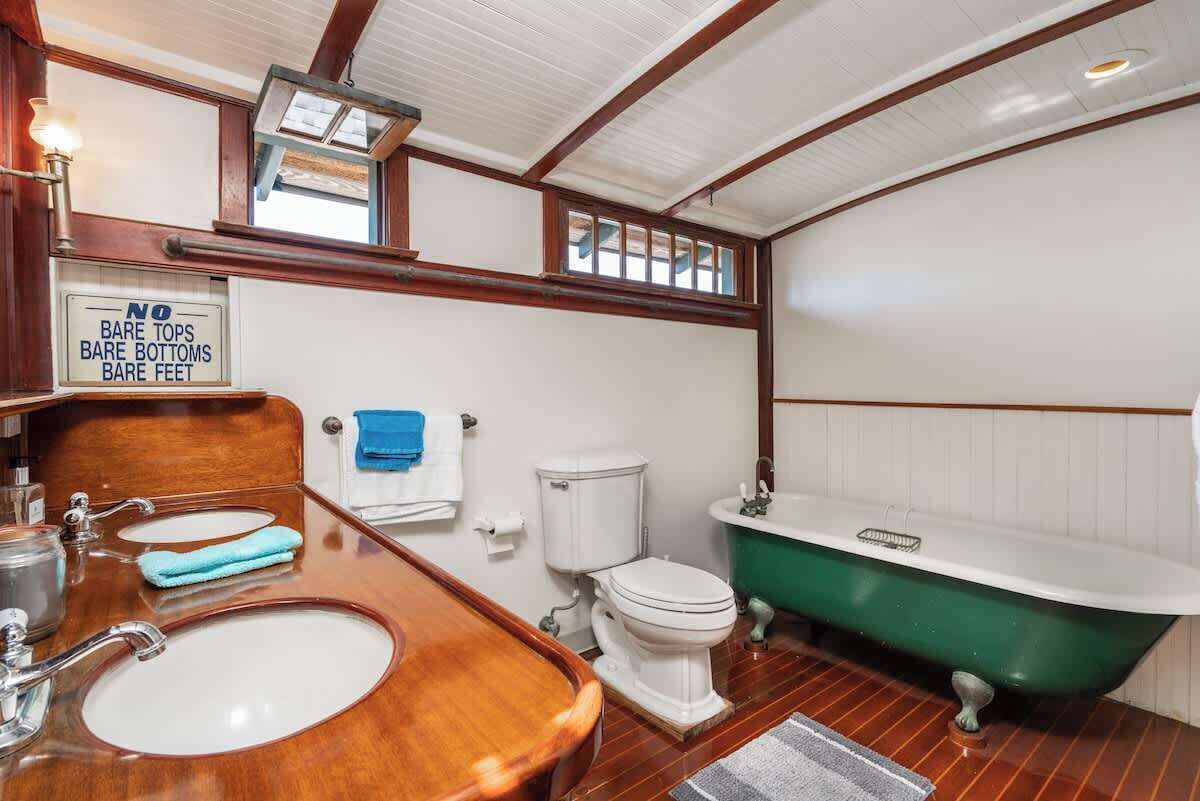 A bathroom with a wooden vanity, two sinks, a toilet, and a green bathtub.