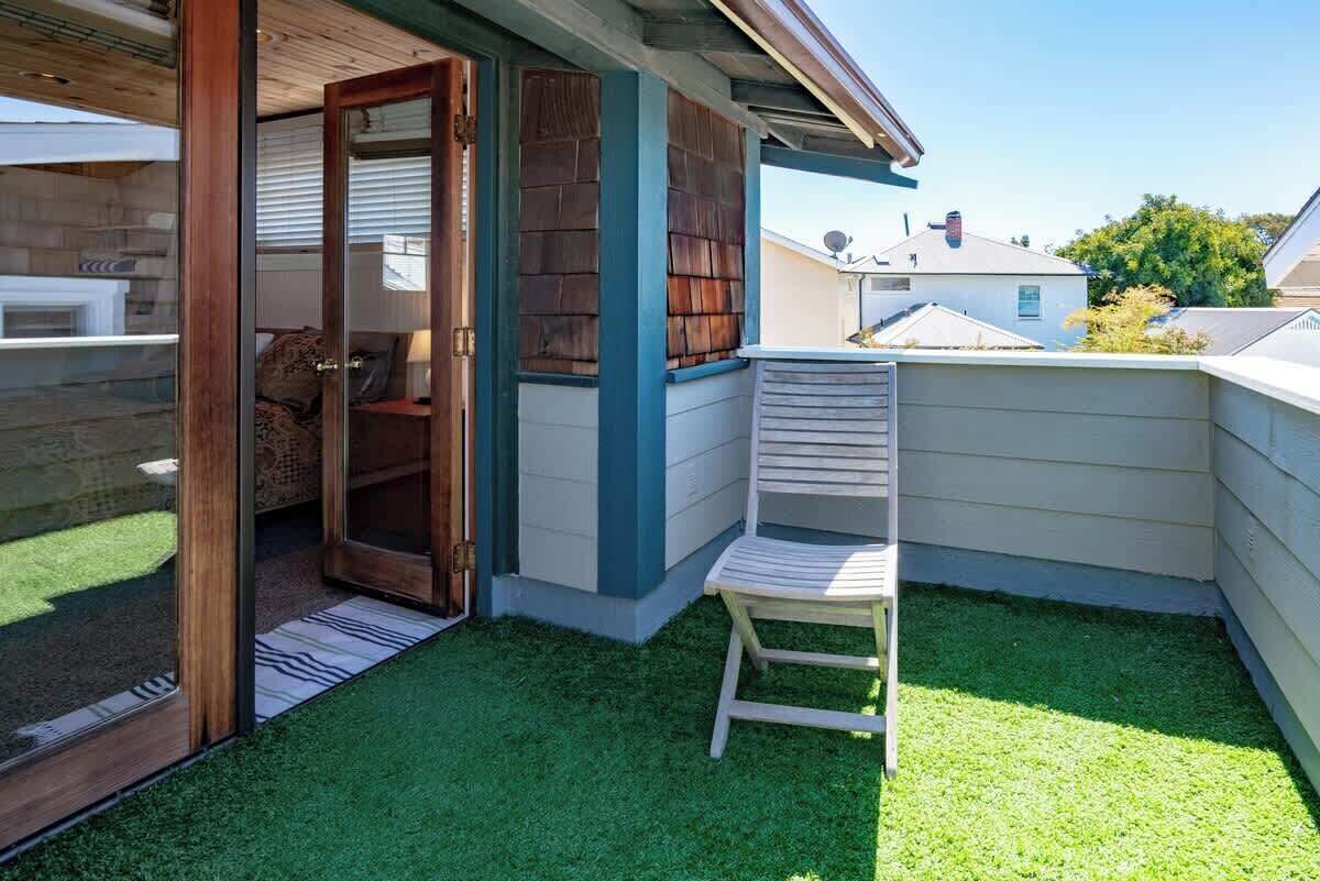 Un petit espace patio clos, avec une chaise en bois, une porte-fenêtre coulissante donnant sur une pièce et une pelouse artificielle verte.