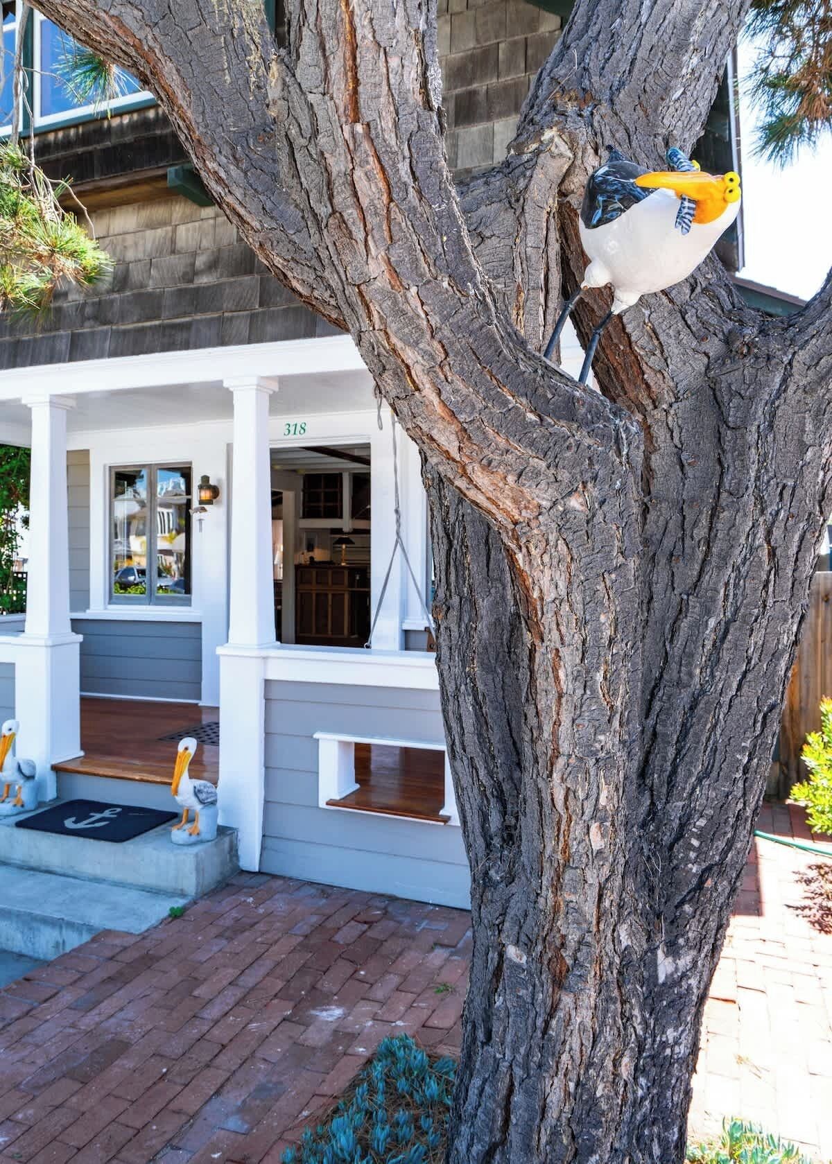 Un árbol con un pájaro posado, un edificio con el número 318 y una puerta con felpudo.