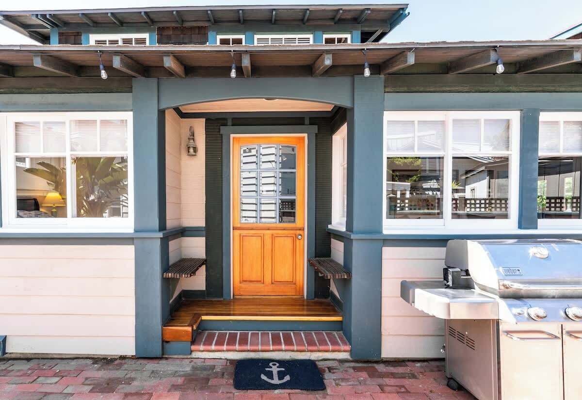 Ein Haus mit einer Holztür, einer Veranda mit Stufen und einem Grill vor der Tür.