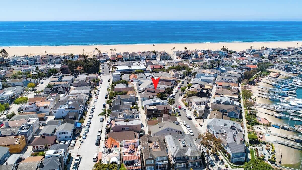 An aerial view of a coastal residential area with a beach, houses, and parked cars.