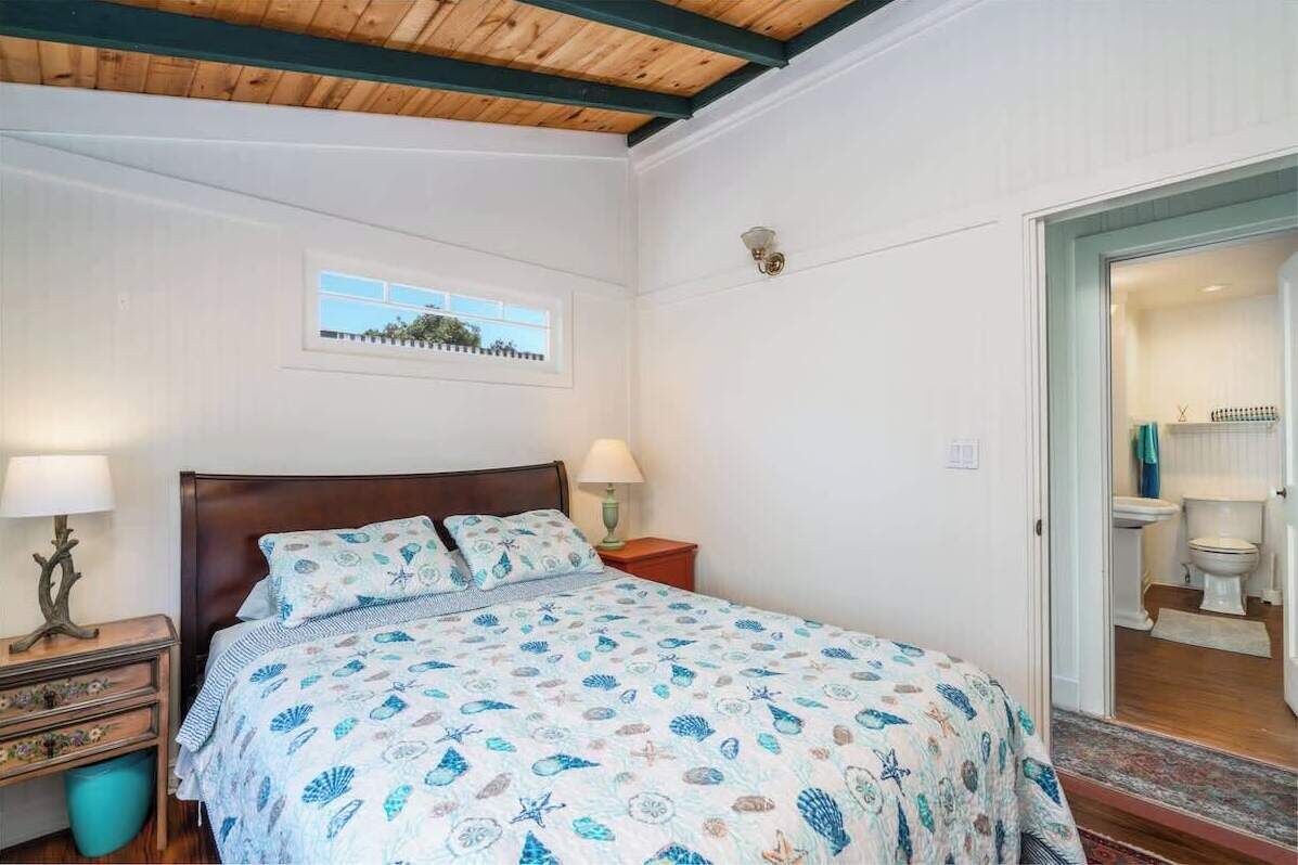 A bedroom with a bed, bedside tables, a window, and a view of the bathroom.