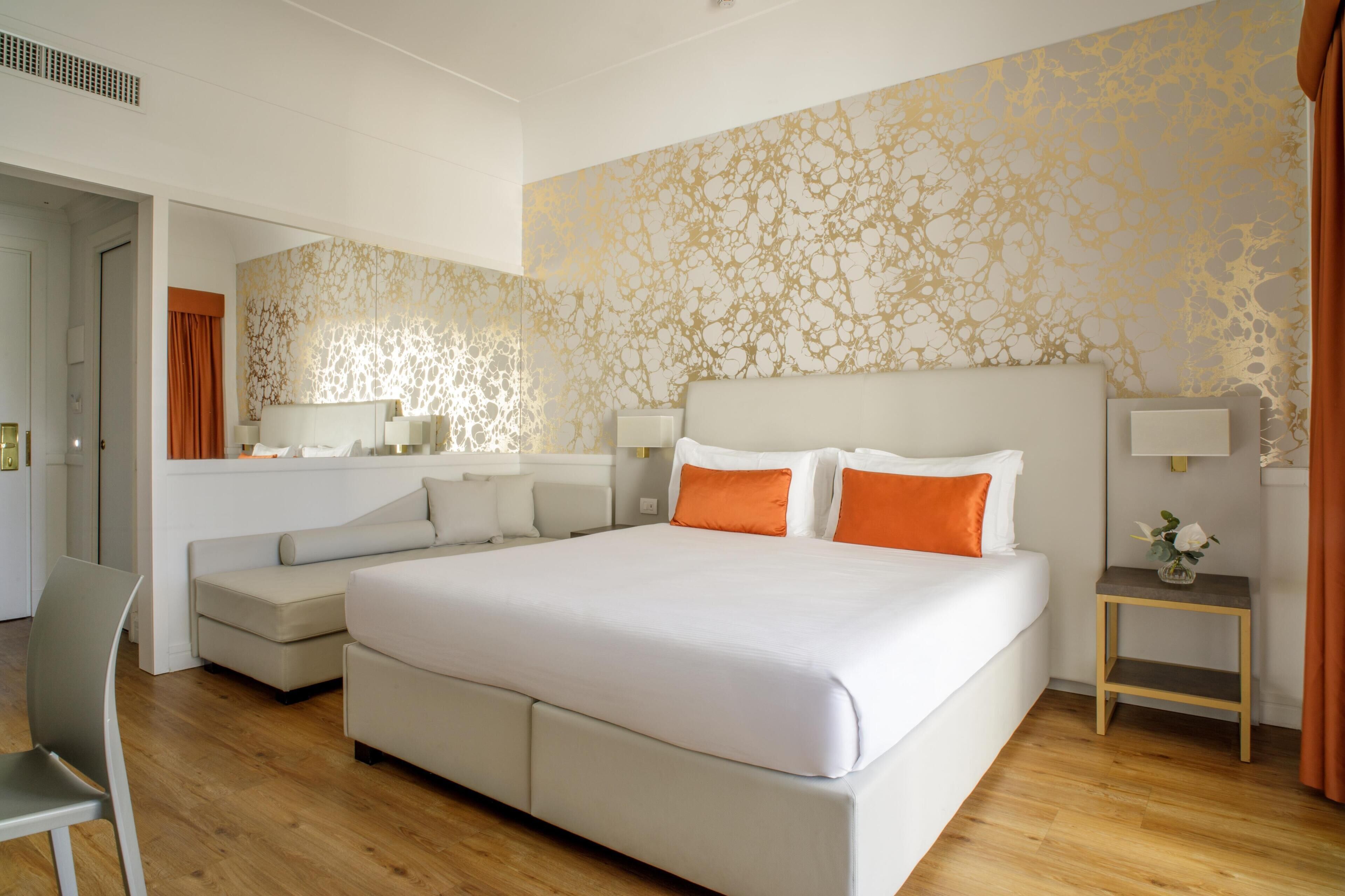 A modern hotel room with a large bed, a sofa, a small table, and a chair.
