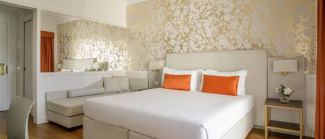 A modern hotel room with a large bed, a sofa, a small table, and a chair.